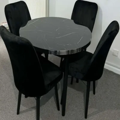 Black round dining table with marble texture top and plush velvet chairs with black wooden legs, perfect for UK homes.